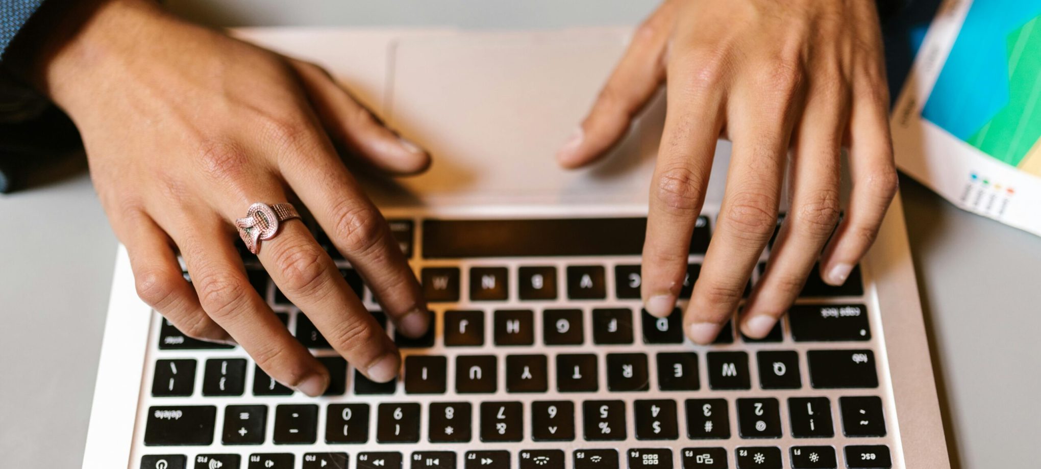 Hands typing on a laptop with a ring, emphasizing technology and work.
